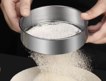 Stainless steel flour sifter being used to sift white flour in a kitchen setting