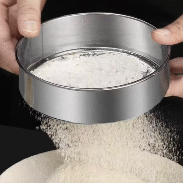 Stainless steel flour sifter being used to sift white flour in a kitchen setting