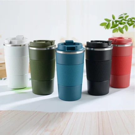 Set of five colorful insulated travel coffee mugs with silicone grips and flip-top lids, arranged on a wooden surface in a bright indoor setting