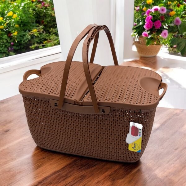 Brown rattan-style plastic picnic basket with lid and handles placed on wooden table near window