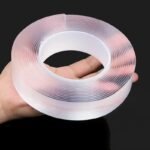 Hand using transparent Nano Magic Double-Sided Adhesive Tape on wooden surface – strong grip reusable tape for wall mounting and home use