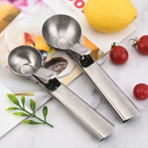 Hand holding a stainless steel ice cream scoop with trigger release over a wooden table