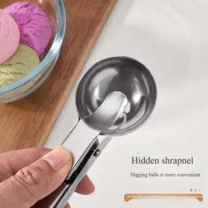 Hand holding a stainless steel ice cream scoop with trigger release over a wooden table